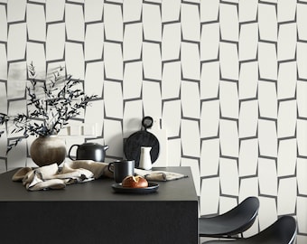 May include: A modern kitchen scene featuring a black countertop with a teapot, mug, and bread roll. A vase with branches and a patterned wallpaper in the background. Black chairs are visible on the right.