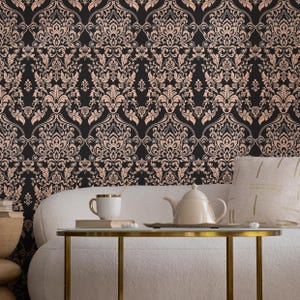 May include: A white couch with a throw pillow sits in front of a black and rose gold damask wallpaper. A gold metal table with a white teapot and a white mug sits on the table.