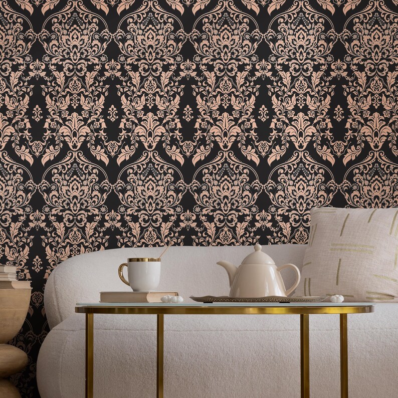 May include: A white couch with a throw pillow sits in front of a black and rose gold damask wallpaper. A gold metal table with a white teapot and a white mug sits on the table.