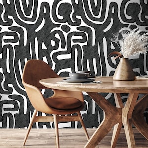 May include: A dining room scene featuring a round wooden table with a brown leather chair. The background is a black and white abstract pattern. A vase with dried flowers and a set of gray dishes are on the table.