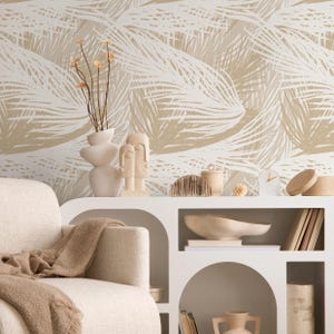 May include: A neutral-toned living room scene featuring a white sofa with a beige throw blanket. A white cabinet displays decorative items like vases, sculptures, and a clock. The backdrop is a wallpaper with a repeating palm leaf pattern in beige and white.