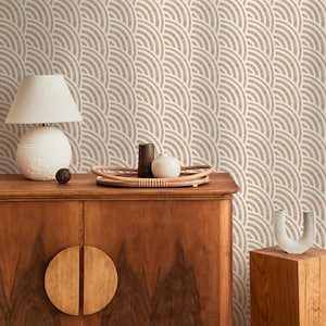 May include: A wooden cabinet with a lamp, decorative tray, and vase. The cabinet has two round wooden handles. The background is a wallpaper with a repeating white and tan semi-circle pattern.