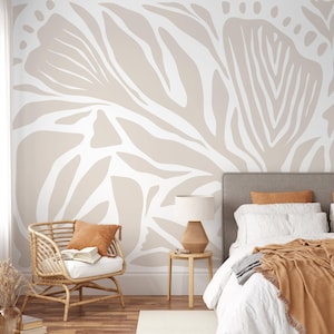 Peut inclure: Une chambre avec une grande murale florale abstraite beige et blanche. Un fauteuil en rotin avec un coussin et une table d'appoint avec une lampe sont au premier plan. Un lit avec des draps blancs et une couverture marron est également visible.