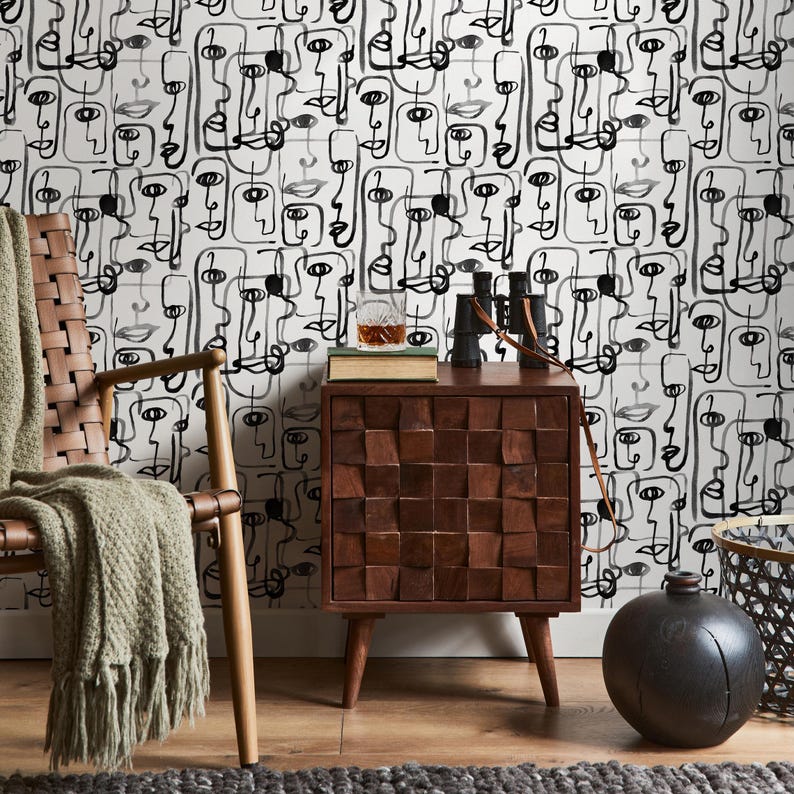 May include: A wooden side table with a unique, textured design. The table has four legs and a single drawer. The table is in front of a wall with a black and white abstract wallpaper featuring faces.