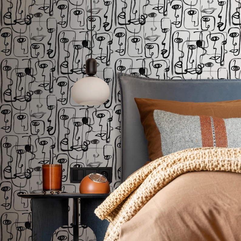 May include: A bedroom with a white and black patterned wallpaper featuring abstract faces. The bed has a brown duvet and a brown throw blanket. A bedside table with a lamp and a clock is next to the bed.