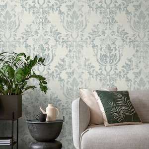 May include: A light blue damask patterned wallpaper with a gray couch and two throw pillows. One pillow is a solid light beige color and the other is a dark green with a fern pattern. A potted plant is in the corner of the image.