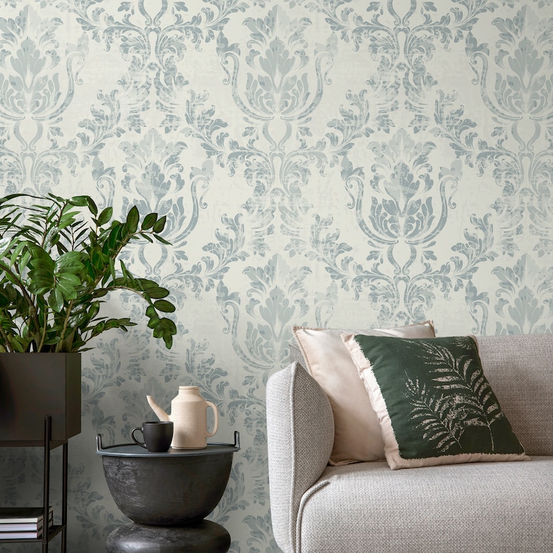 May include: A light blue damask patterned wallpaper with a gray couch and two throw pillows. One pillow is a solid light beige color and the other is a dark green with a fern pattern. A potted plant is in the corner of the image.