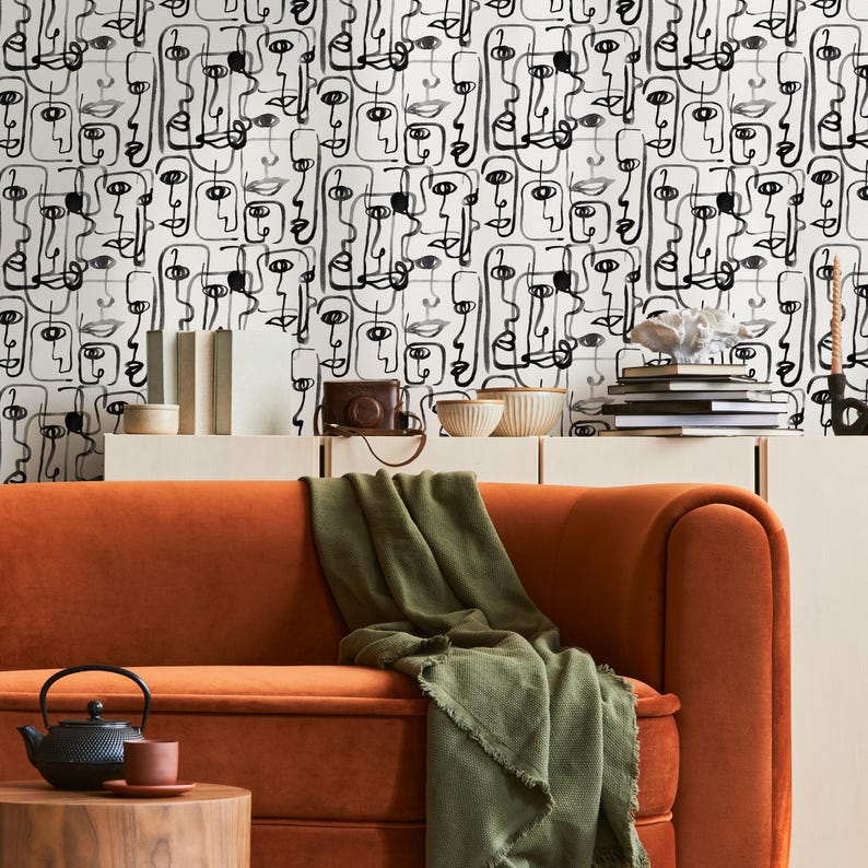 May include: A living room with an orange couch and a green throw blanket. The wall behind the couch is covered in black and white abstract wallpaper with a pattern of faces.