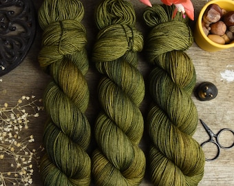 May include: Three skeins of yarn in shades of green and brown. The yarn is arranged in a vertical line, with the skeins stacked on top of each other.