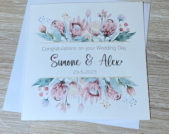 May include: A white wedding card with a watercolor illustration of pink protea flowers and greenery. The card reads "Congratulations on your Wedding Day Simone & Alex 23-5-2023".