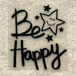 Könnte beinhalten: Schwarzer Vinyl-Aufkleber mit den Worten "Be Happy" in handschriftlicher Form. Ein lächelnder Stern mit fünf Zacken befindet sich über den Worten, umgeben von kleineren Sternen.