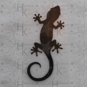 Könnte beinhalten: Schwarze Metall-Gecko-Silhouette als Wanddekoration. Der Gecko ist in einer Ruheposition zusammengerollt, mit dem Schwanz um den Körper gewickelt. Der Gecko ist ein beliebtes Symbol für Glück und Wohlstand.
