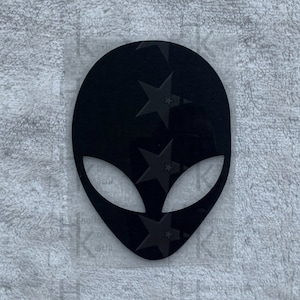 Könnte beinhalten: Schwarze Alien-Kopf-Silhouette mit glatter, glänzender Oberfläche. Der Alien-Kopf ist ein beliebtes Design für Aufkleber, Abziehbilder und Bügelbilder.