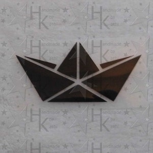 Könnte beinhalten: Schwarzes Papier-Origami-Boot mit gefaltetem Design. Das Boot befindet sich auf einem weißen Hintergrund mit einem sich wiederholenden Muster aus Sternen und dem Text "handmade by athi".