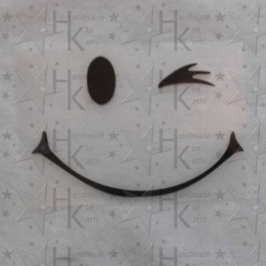 Könnte beinhalten: Ein schwarz-weißes Smiley-Gesicht, das mit einem schwarzen Auge zwinkert und einen geschwungenen Mund hat. Der Hintergrund ist eine weiße Oberfläche mit einem sich wiederholenden Muster aus schwarzen Sternen und dem Text "handmade by athi".