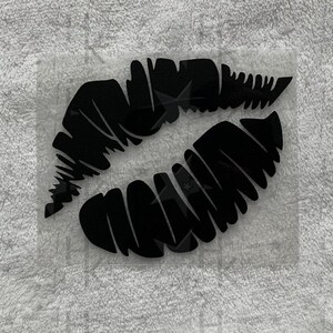 Könnte beinhalten: Ein schwarzer Vinyl-Aufkleber mit einem Paar Lippen. Die Lippen sind schwarz umrandet und haben eine strukturierte Optik.