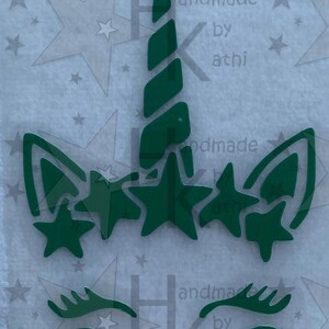 Könnte beinhalten: Grüne Einhorn-Silhouette mit einem spiralförmigen Horn und fünf Sternen. Das Einhorn hat Wimpern und eine runde Nase.