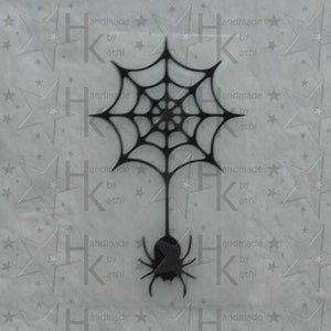 Könnte beinhalten: Schwarze Spinnennetz- und Spinnen-Dekoration. Das Spinnennetz ist aufwendig gestaltet mit einer zentralen Spirale und radialen Linien. Die Spinne hängt unter dem Netz. Der Hintergrund hat ein sich wiederholendes Sternmuster und den Text "handmade by athi".
