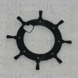 May include: Black wooden ship's wheel with a small heart cutout in the center. The wheel has eight spokes and a circular rim.