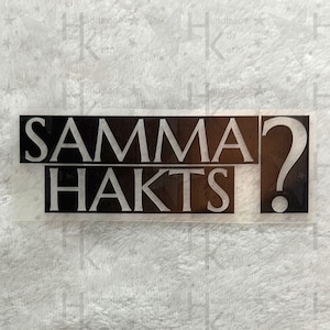 Könnte beinhalten: Schwarz-weißer Vinyl-Aufkleber mit dem Text "SAMMA? HAKTS!" in einer fetten, serifenlosen Schrift.