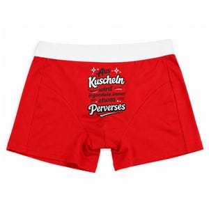 May include: Bright red boxer briefs featuring a wide white elastic waistband. The front of the garment displays black text that reads "Aus Kuscheln wird irgendwie immer etwas Perverses" with decorative star accents and horizontal lines.