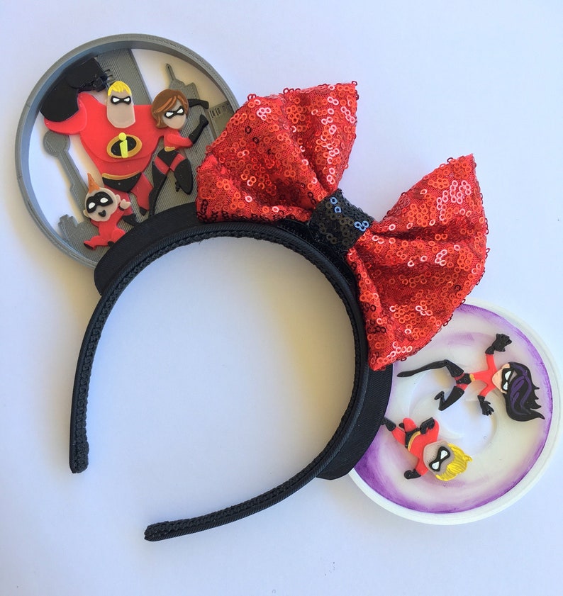 May include: Red sequin Minnie Mouse ears with a black headband. The ears feature a 3D image of the Incredibles family in front of a cityscape.