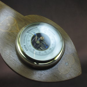 Può includere: Un barometro in legno con un quadrante in ottone e una copertura in vetro. Il quadrante ha uno sfondo bianco con segni neri e un ago blu. Il barometro indica "STORM" e "VERY DRY".