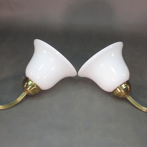 May include: A pair of brass wall sconces with white glass shades. The sconces have a curved arm and a decorative base.