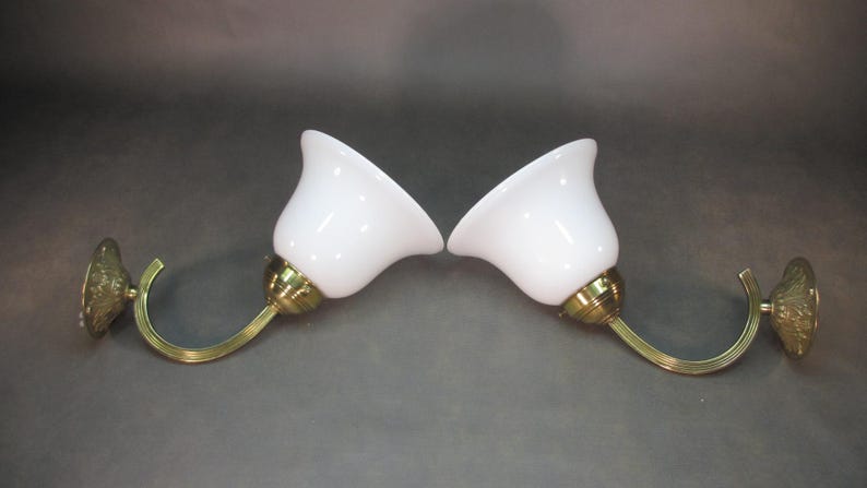 May include: A pair of brass wall sconces with white glass shades. The sconces have a curved arm and a decorative base.