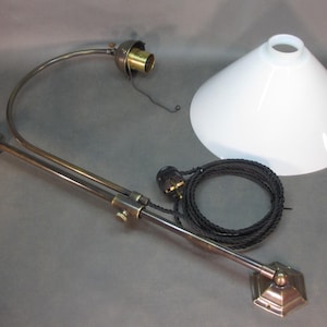 May include: A brass wall-mounted lamp with a white cone-shaped shade and a black cord. The lamp has a swivel arm and a decorative base.