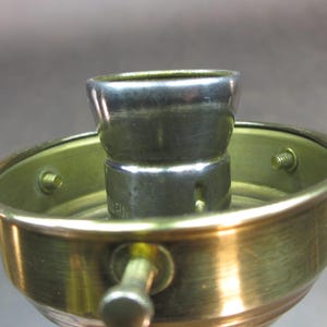May include: Close-up of a brass lamp socket with a silver metal light bulb holder.