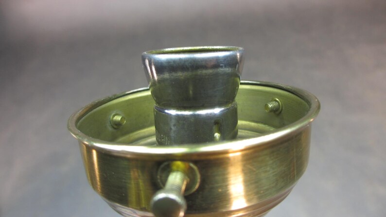 May include: Close-up of a brass lamp socket with a silver metal light bulb holder.