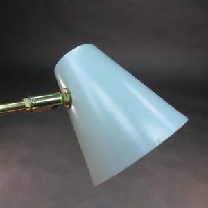 Pu&ograve; includere: Una lampada da tavolo regolabile in ottone e blu chiaro con un paralume a forma di cono.