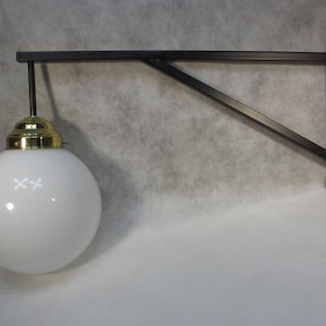 Könnte beinhalten: Eine schwarze Wandleuchte aus Metall mit einem weißen Globus-Schirm. Die Leuchte hat ein schlichtes, industrielles Design.