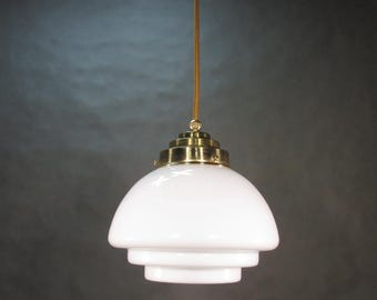 May include: A white glass pendant light with a brass fixture. The light has a layered, tiered design.