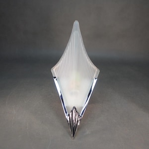 May include: A vintage wall sconce with a frosted glass shade in a diamond shape. The shade has vertical lines radiating from the center. The sconce has a chrome-colored metal trim and base, creating a classic art deco design.