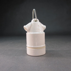 May include: A vintage, off-white ceramic light fixture socket with two side openings and a metal loop for hanging. The socket has a cylindrical base and a slightly textured surface, perfect for a retro or industrial aesthetic.