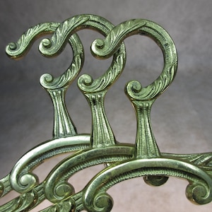 May include: Three ornate gold-toned metal hangers with decorative scrollwork and a hook at the top.