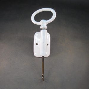 May include: White porcelain wall-mounted hook with a ring handle and a metal hook.