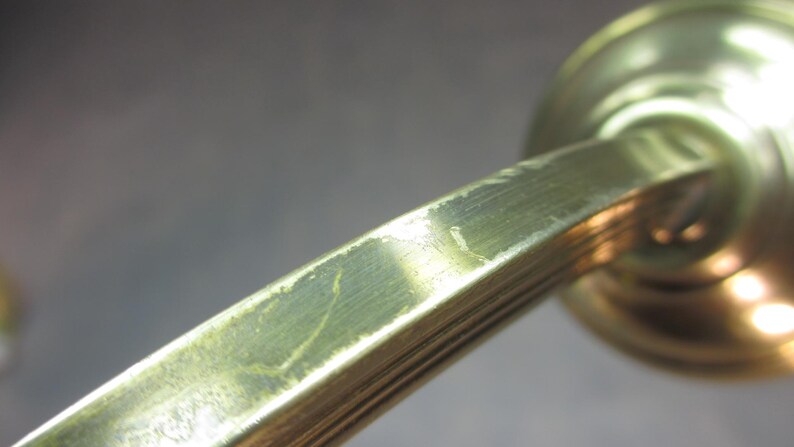 May include: A close-up of a brass door handle with a smooth, polished finish. The handle has a rounded shape and a long, slender arm.