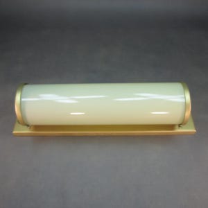 Peut inclure: Un luminaire cylindrique avec un tube en verre jaune pâle et une garniture en métal doré. Le luminaire est monté sur une base rectangulaire dorée. Le design est simple et moderne.