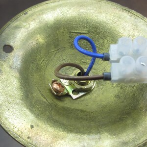 May include: Close-up of a brass ceiling fixture with a white plastic wire connector and blue and brown wires. The fixture has a round, recessed opening for a light bulb.