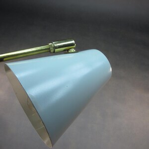Pu&ograve; includere: Una lampada da scrivania vintage in ottone e metallo blu con un paralume a forma di cono. La lampada ha un braccio flessibile e una testa girevole.