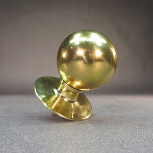 Puede incluir: Un pomo de puerta de latón pulido con una manija redonda y esférica y una base plana y circular.