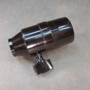 Könnte beinhalten: Ein dunkelbraunes, zylindrisches Objekt mit einem ausgestellten Ende und einer kleinen, verstellbaren Flügelmutter. Das Objekt hat eine Reihe von Rillen und einen kleinen Schlitz. Der Artikel scheint aus einem harten, möglicherweise Kunststoffmaterial zu bestehen.