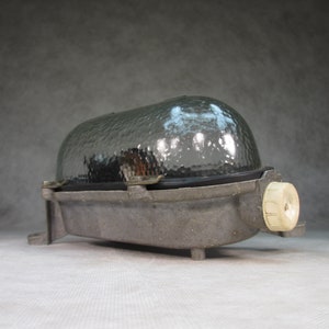 May include: A vintage industrial style light fixture with a frosted glass shade and a metal housing. The fixture has a white plastic electrical outlet on the side.