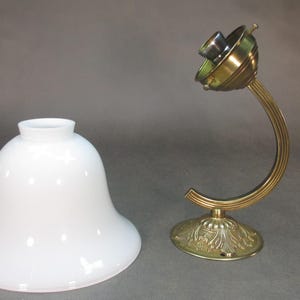 May include: A white glass lampshade with a bell shape and a brass lamp base with a curved arm.