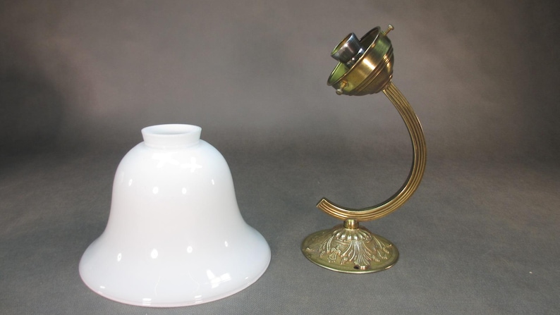 May include: A white glass lampshade with a bell shape and a brass lamp base with a curved arm.