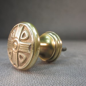 Może przedstawiać: Mosiężny gałka do szafki z ozdobnym, geometrycznym wzorem. Gałka ma okrągłą podstawę i śrubę do mocowania do drzwi szafki.