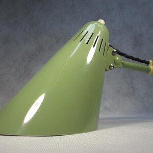 Könnte beinhalten: Eine grüne Metall-Tischlampe mit einem konischen Schirm und einem flexiblen Arm. Die Lampe hat einen weißen Knopf oben und ein schwarzes Kabel.